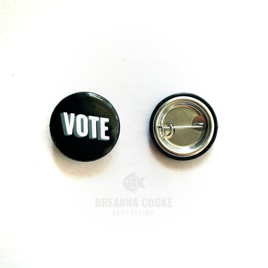 Pin-back black button with word "VOTE" on black background.