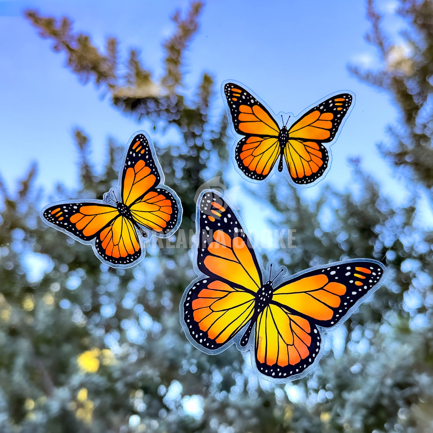 Three orange and black monarch butterflies against a blurred natural background